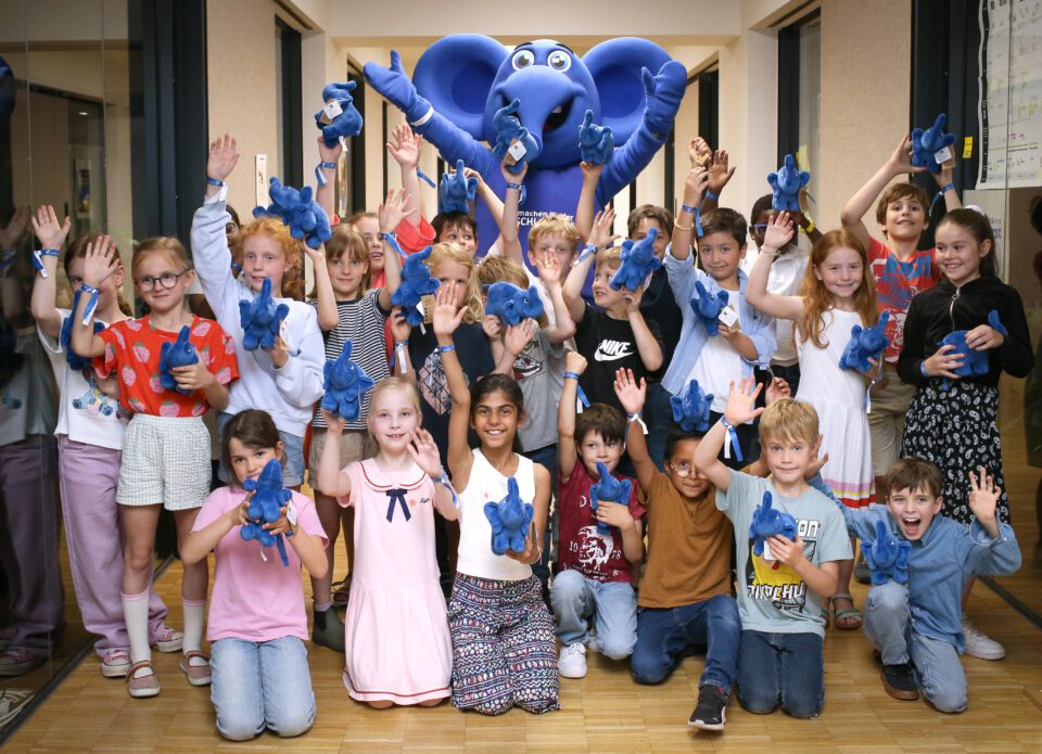 Kinder mit blauem Elefant, eine Hand in die Luft gestreckt, jedes Kind hält einen kleinen blauen Elefanten in der Hand und