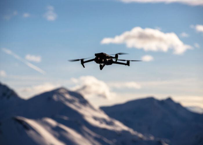A drone flies over scenic snow-covered peaks under a clear blue sky, capturing breathtaking landscapes.